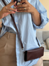 Person wearing a light blue shirt and beige pants, holding a phone with a floral case and carrying markore gul sahar crossbody bag handmade from full-grain leather