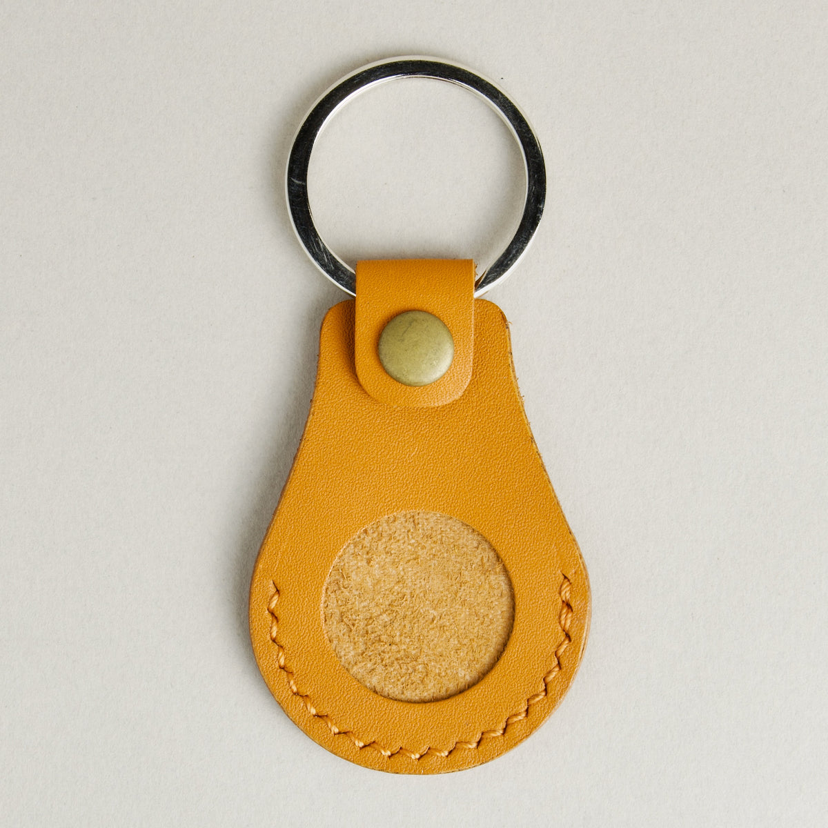Front view of amber AirTag keychain in full-grain leather with round metal key ring and brass press stud. Markore Tag Mate.