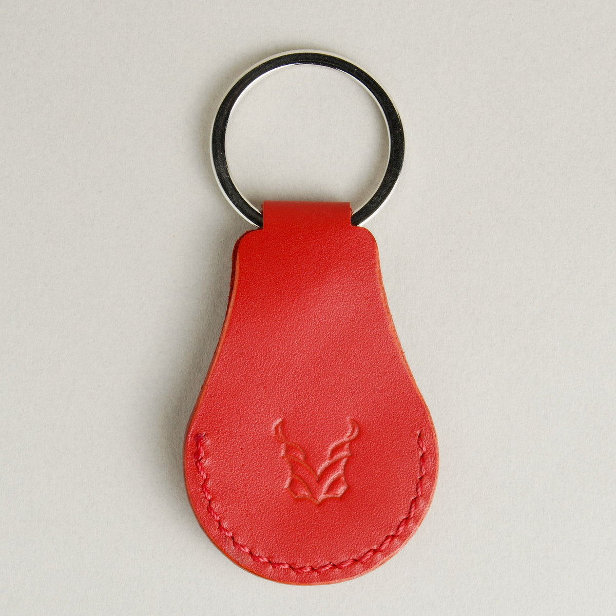 Back view of red AirTag keychain in full-grain leather with round metal key ring and embossed logo. Markore Tag Mate.