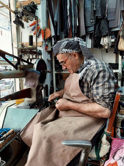 Artisan working at a sewing machine in a workshop with various tools and fabrics around.