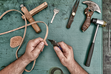 Artisan working with leather and leather tools on a green work space