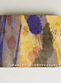 Front view of hand-painted full-grain leather bifold wallet in purple, amber, and brown, featuring handmade stitching. Markore Canvas Chaos.