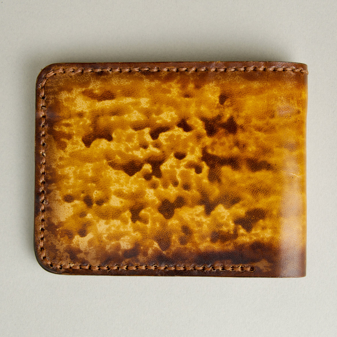 Backside view of hand-painted full-grain leather bifold wallet in amber and brown, featuring handmade stitching. Markore Canvas Flame.