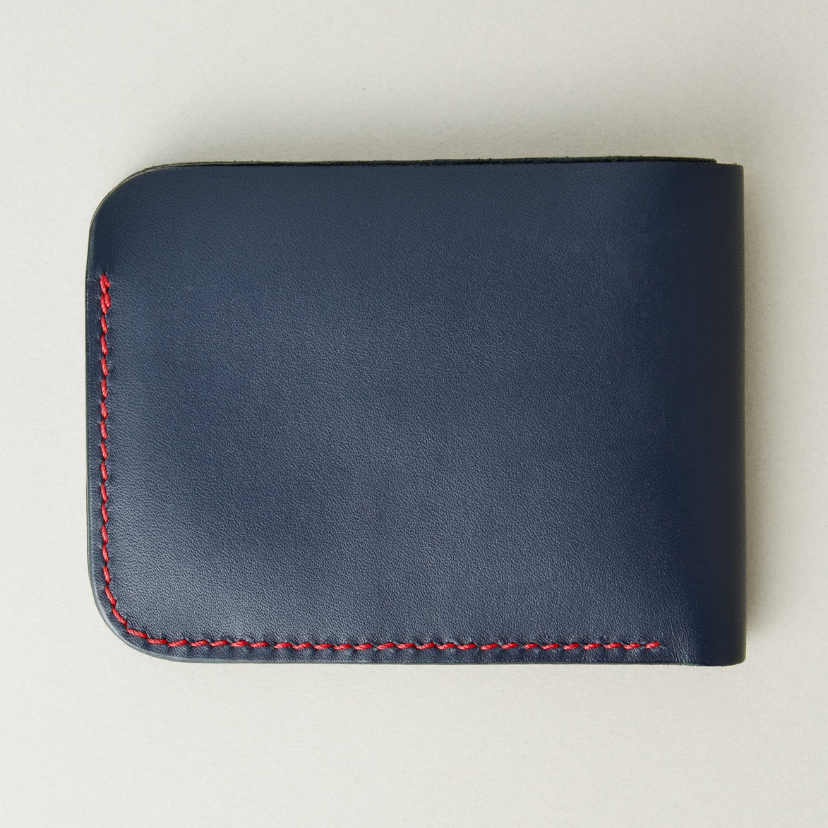 Back view of full-grain leather bifold wallet with hand-stitched red thread in Dark Blue and embossed logo. Markore Hunza Arc.