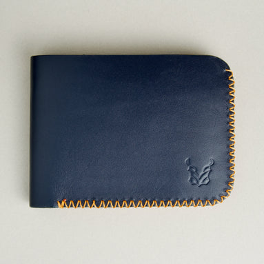 Front view of dark blue full-grain leather bifold wallet featuring handmade amber cross-stitched detailing on the edges and embossed logo. Markore Hunza Edge.