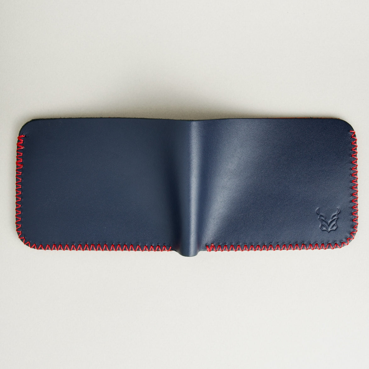 Back view of unfolded dark blue full-grain leather bifold wallet featuring handmade red cross-stitched detailing on the edges. Markore Hunza Edge.