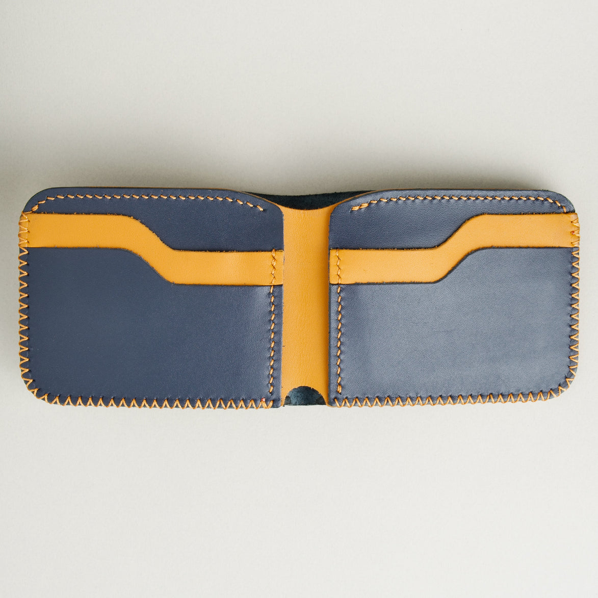 Open view of Dark Blue and amber full-grain leather bifold wallet featuring card slots and amber hand-stitched detailing. Markore Hunza Edge.