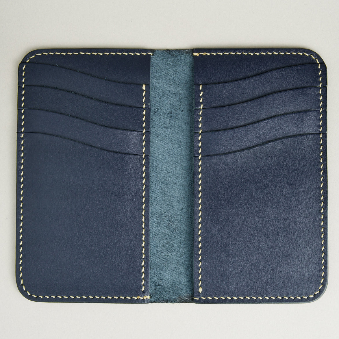Inside view of vertical full-grain leather bifold wallet in dark blue, with cards lots and handmade stitching. Markore Karakoram II.