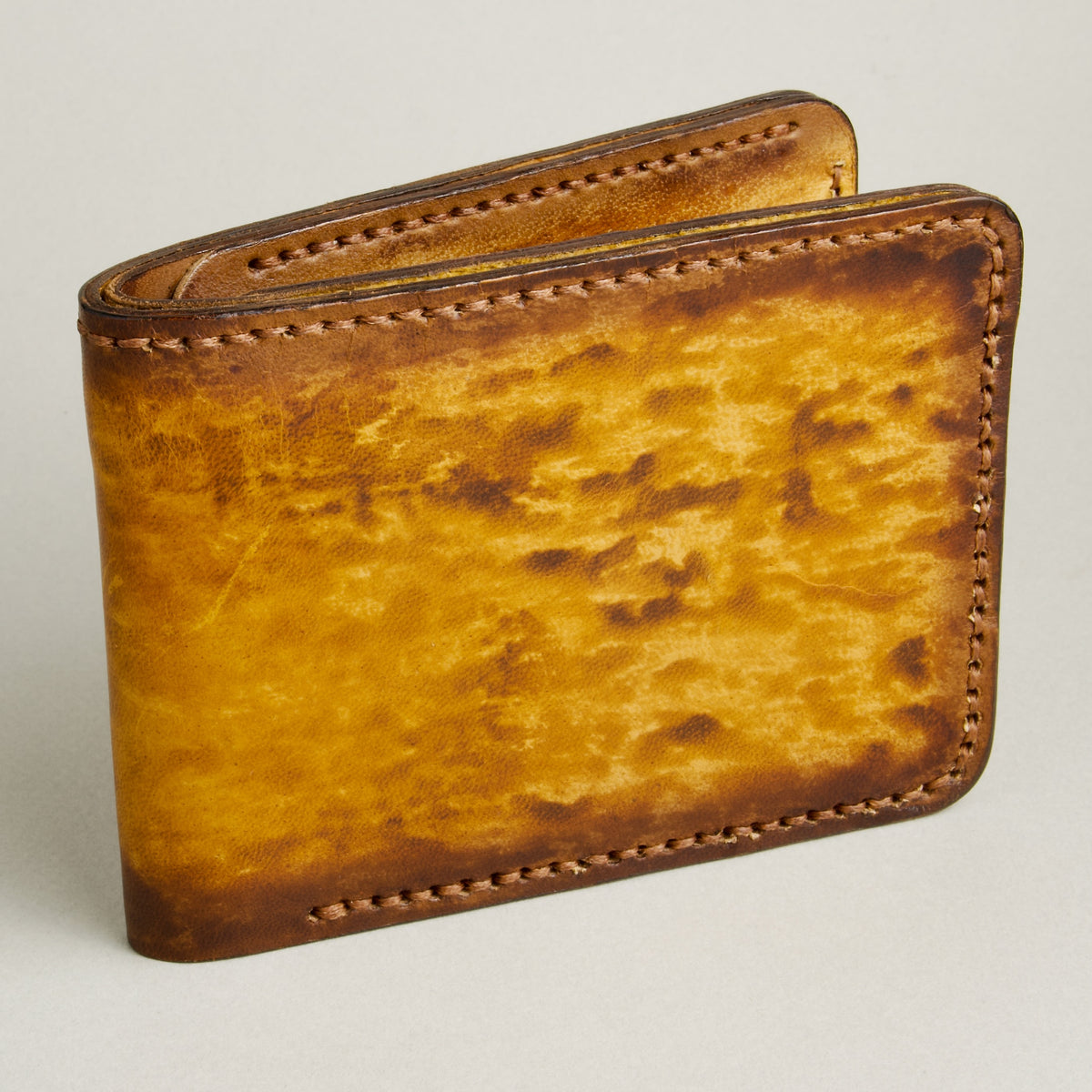 Side view of hand-painted full-grain leather bifold wallet in amber and brown, featuring handmade stitching. Markore Canvas Flame.