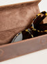 Tortoiseshell sunglasses resting inside an open brown leather case with a suede-like brown interior, photographed on a clean white background.