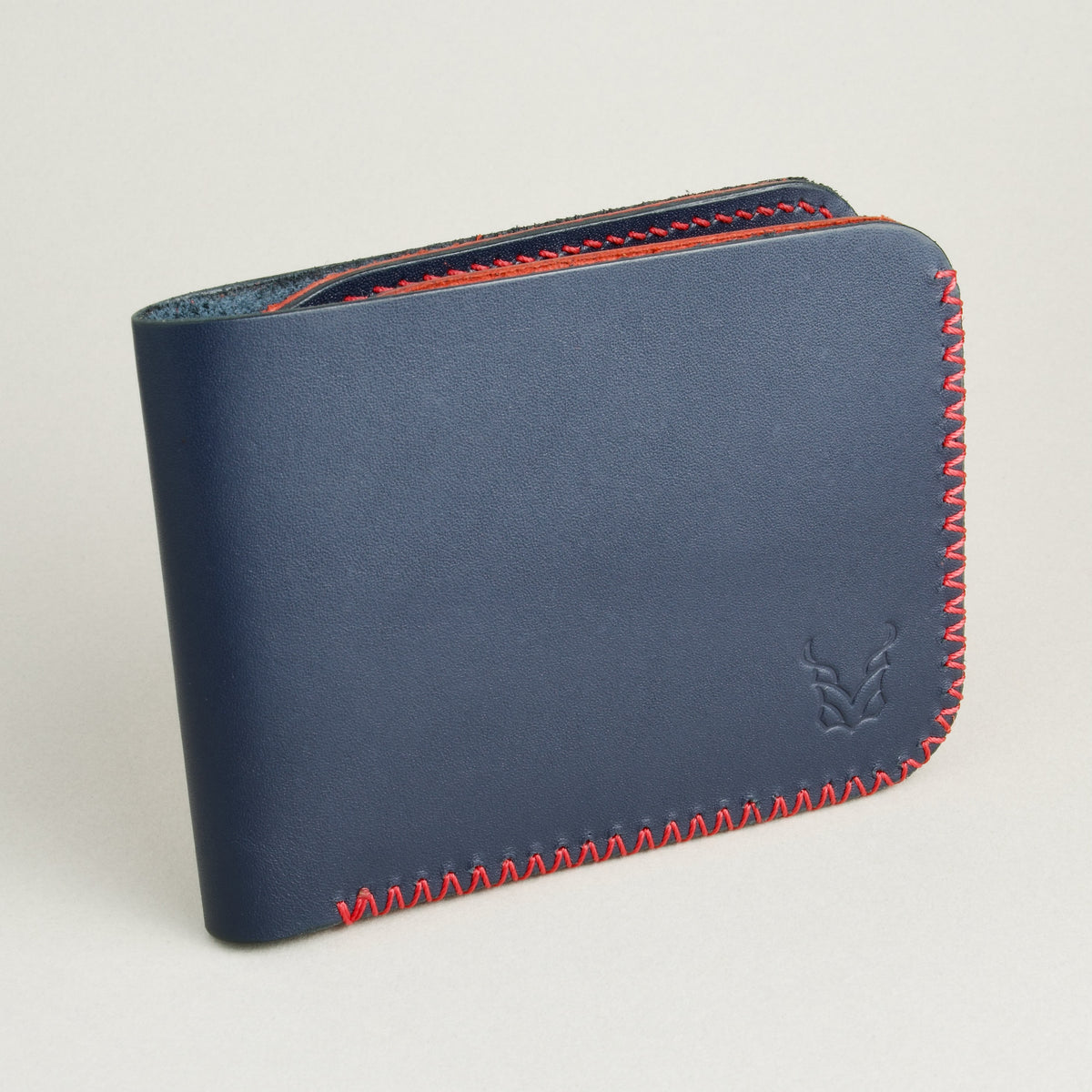 Side view of dark blue full-grain leather bifold wallet featuring handmade red cross-stitched detailing on the edges and embossed logo. Markore Hunza Edge.