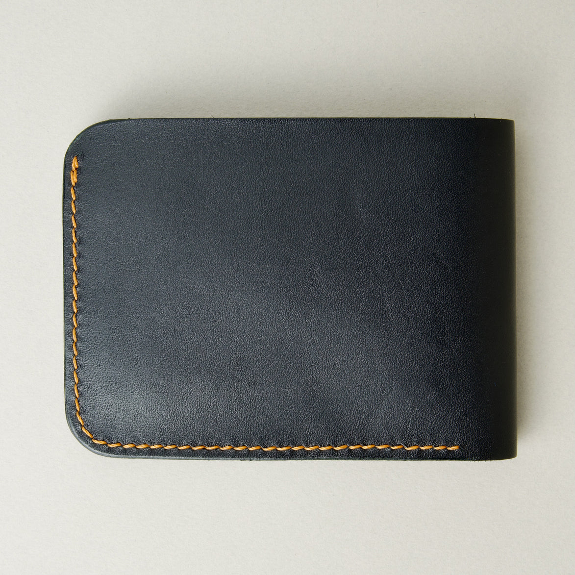 Back view of full grain leather bifold wallet in midnight black, featuring handmade stitching in amber. Markore Hunza Fold.
