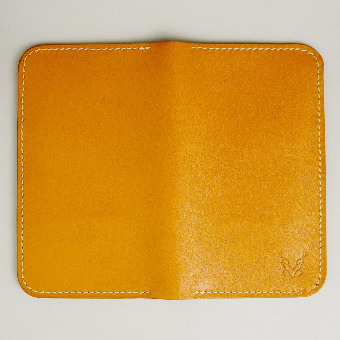 Unfolded back view of vertical full-grain leather bifold wallet in Amber, with handmade stitching and embossed logo. Markore Karakoram II.