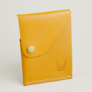 Side view of full grain leather card in amber with ivory handmade stitching, featuring a flap with brass press button and embossed logo. Markore Niva Heritage.