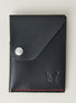Front view of full grain leather card holder in black with red handmade stitching, featuring a flap with stainless steel press button and embossed logo. Markore Niva Heritage.