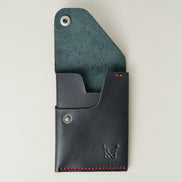 Front view of full grain leather card in black with red handmade stitching, with an open flap with stainless steel press button, card slots and embossed logo. Markore Niva Heritage.