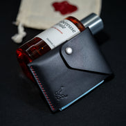 markore niva heritage ultra compact card sleeve in midnight black with red stitching resting on a perfume bottle on a black surface with markore canvas packaging in the background  