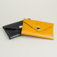 Side view of two full grain leather envelope style wallets in midnight black and amber with stainless steel button and embossed logo. Markore Niva Seal.