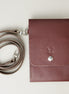 Front view of vertical full-grain leather crossbody bag and matching shoulder strap in Espresso Brown, showing handmade stitching, embossed logo and stainless steel press stud. Markore Nora Veldt.