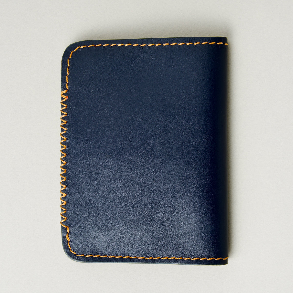 Back view of dark blue full-grain leather wallet highlighting amber handmade cross stitch detailing along the edge. Markore Ravi Edge.