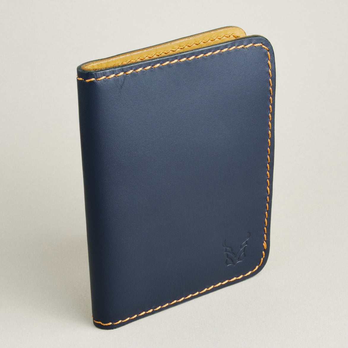 Side view of dark blue full-grain leather wallet highlighting the amber handmade stitching and embossed logo. Markore Ravi Edge.