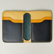 Inside view of black full-grain leather wallet revealing tri-tone interior pockets in black, amber and yellow, featuring amber handmade stitching. Markore Ravi Fold.