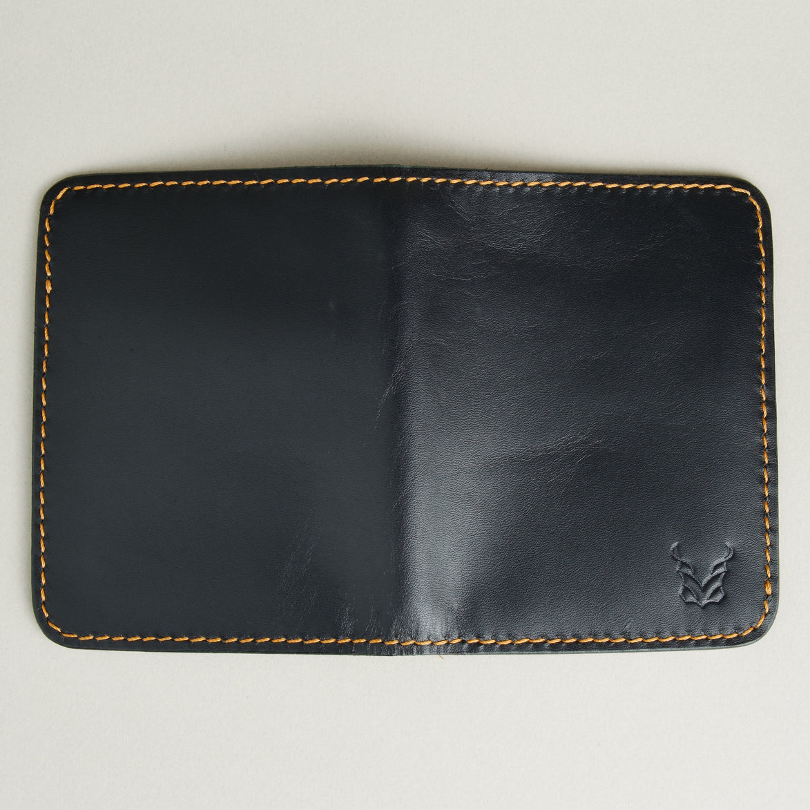 Outside view of midnight black full-grain leather vertical wallet featuring amber handmade stitching and embossed logo. Markore Ravi Fold.