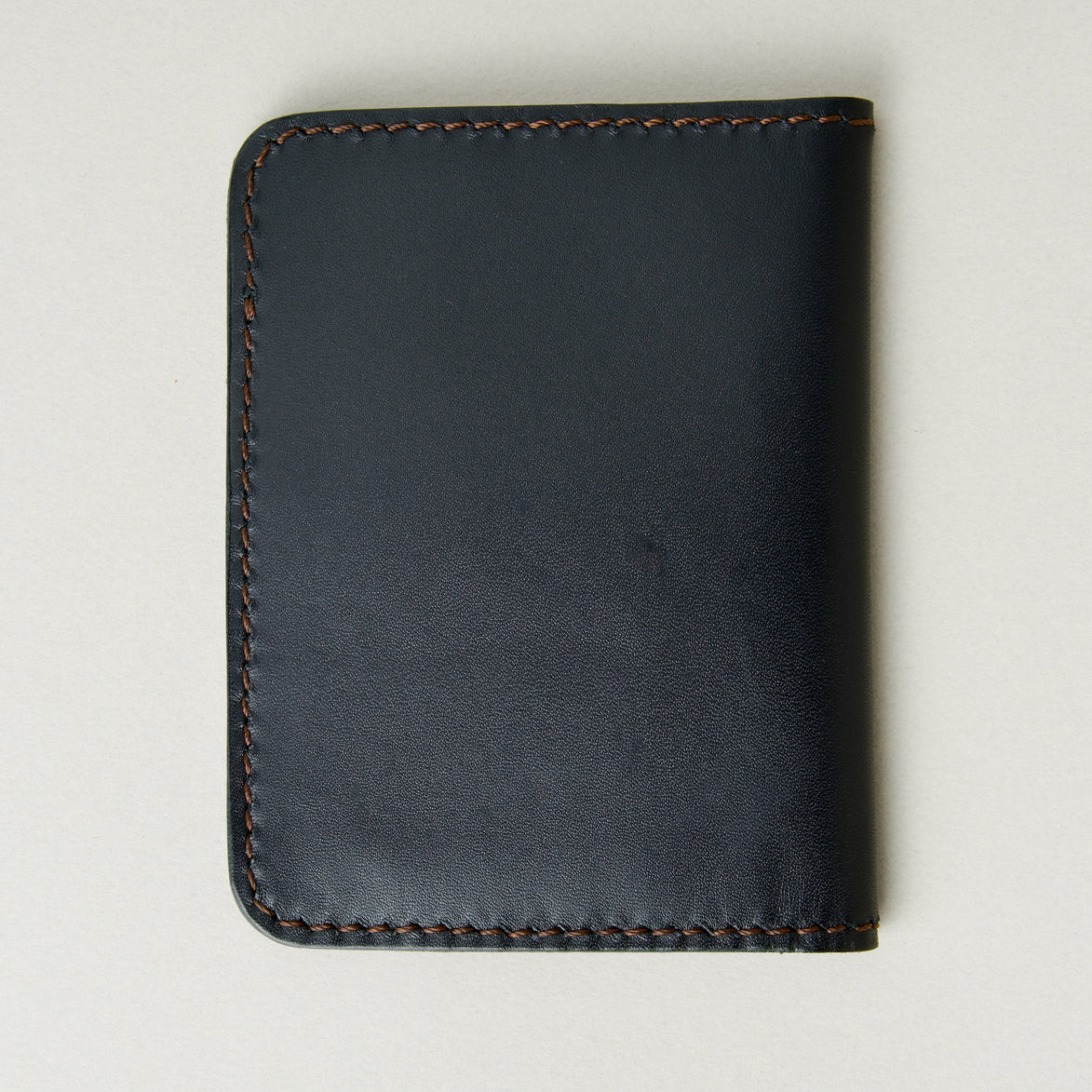 Back view of midnight black full-grain leather wallet featuring espresso brown handmade stitching. Markore Ravi Fold.