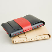 Side view of two full-grain leather flap wallets in midnight black with red and natural, featuring a flap holder with embossed logo, and handmade stitching. Markore Sutlej Vault.