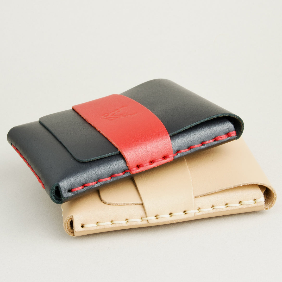 Side view of two full-grain leather flap wallets in midnight black with red and natural, featuring a flap holder with embossed logo, and handmade stitching. Markore Sutlej Vault.