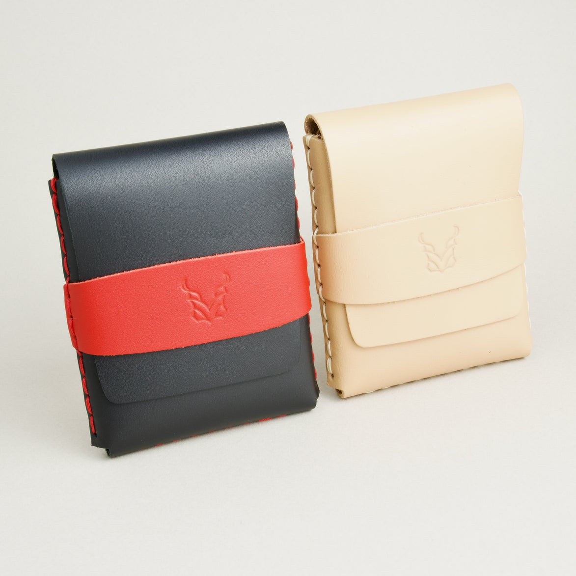 Two full-grain leather flap wallets in midnight black with red and natural, featuring a flap holder with embossed logo, and handmade stitching. Markore Sutlej Vault.