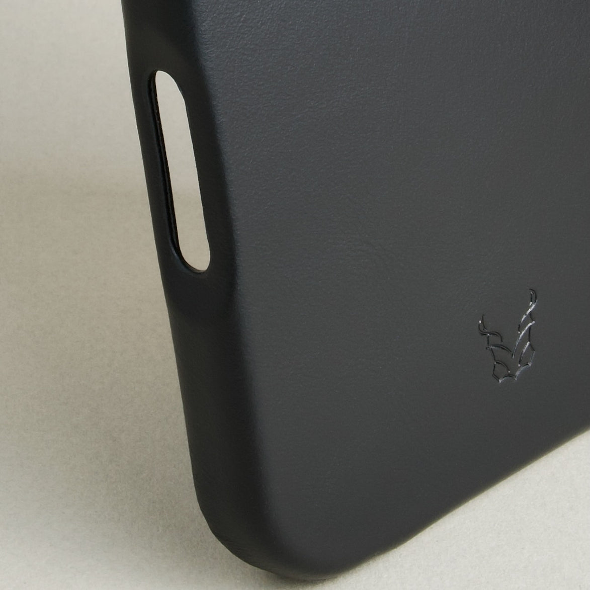 Detail of midnight black leather iphone 17 pro case featuring button cutout and embossed logo. Markore Shell Frame.