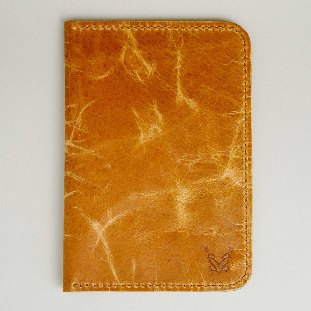 Front view of vertical full-grain leather passport holder in amber, featuring handmade stitching and embossed logo. Markore Voyage Pass.
